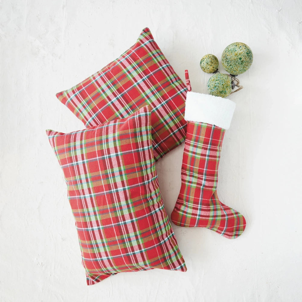 Red tartan plaid Christmas stocking, two matching throw pillows, and green ornaments on a white surface.