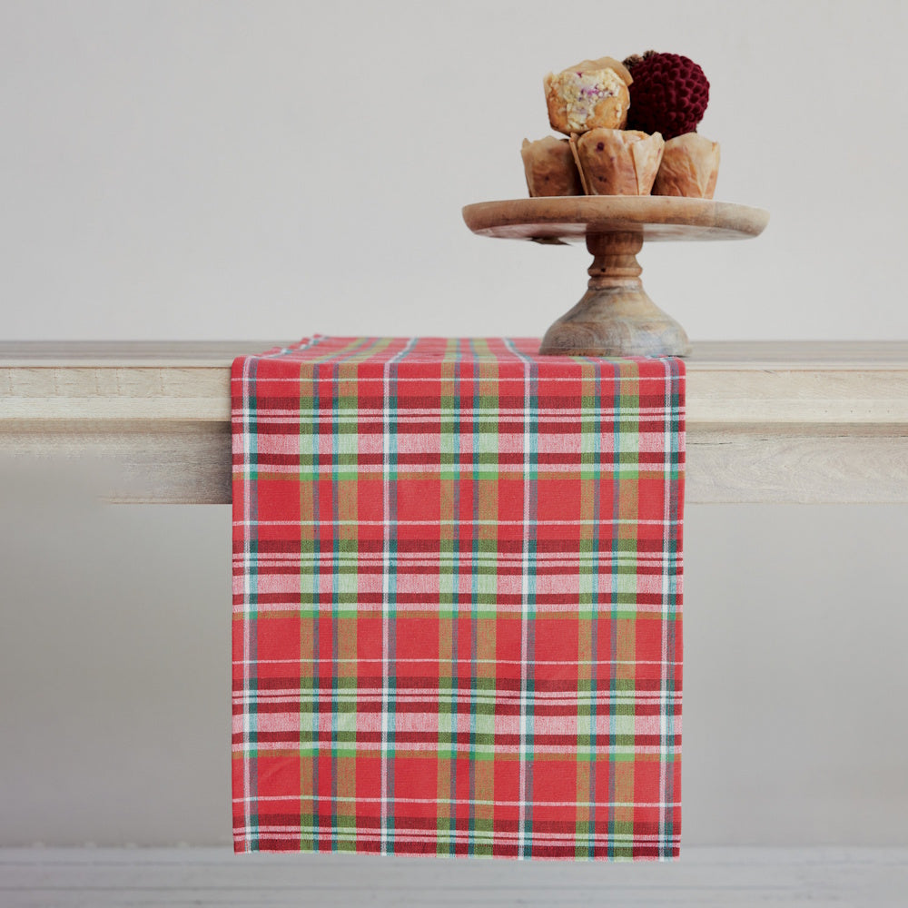Woven cotton table runner featuring a vibrant red tartan plaid pattern draped over a wooden table beneath a wooden cake stand.