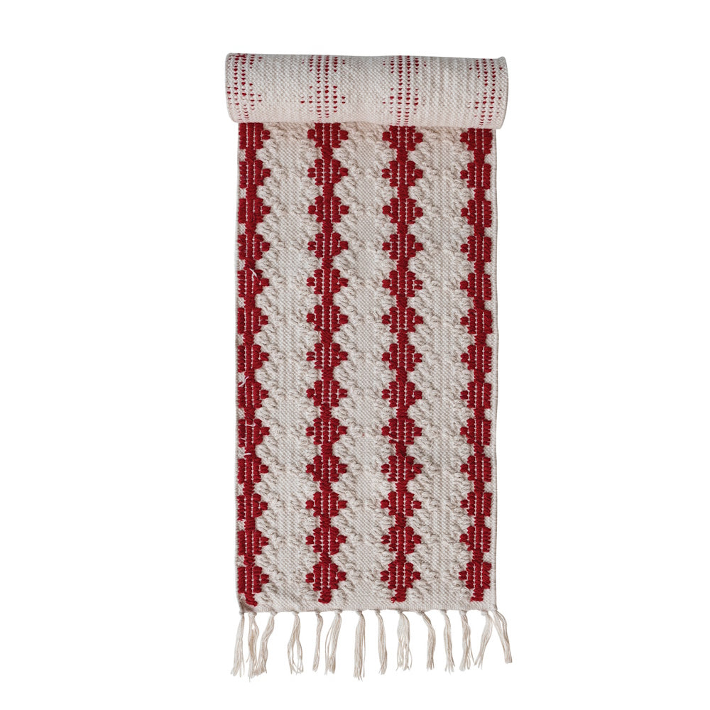 Rolled woven white and red patterned table runner with fringe at the bottom edge.
