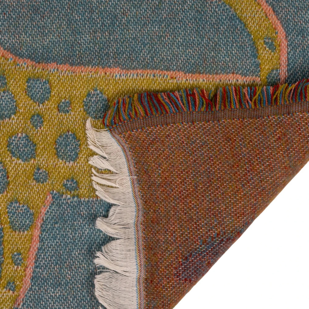 Close-up of a woven leopard throw blanket folded over to show the yellow pattern, fringed edge, and back side.