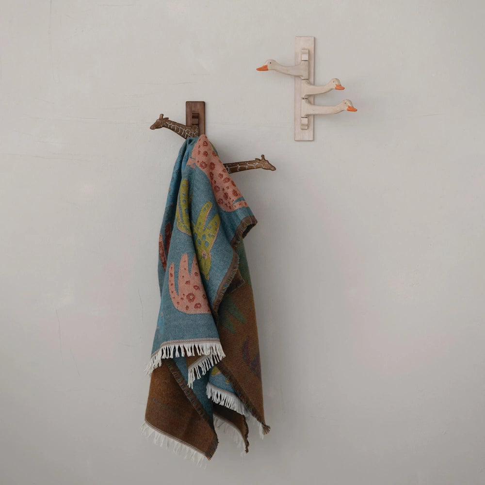 Teal woven leopard throw blanket hanging on a wooden giraffe wall hook in a neutral-toned room.