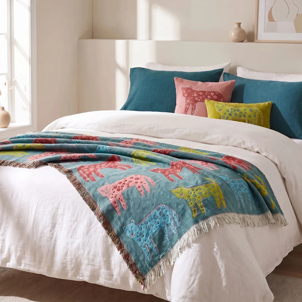 Teal woven leopard throw blanket draped over the foot of a bed with white bedding and accent pillows.