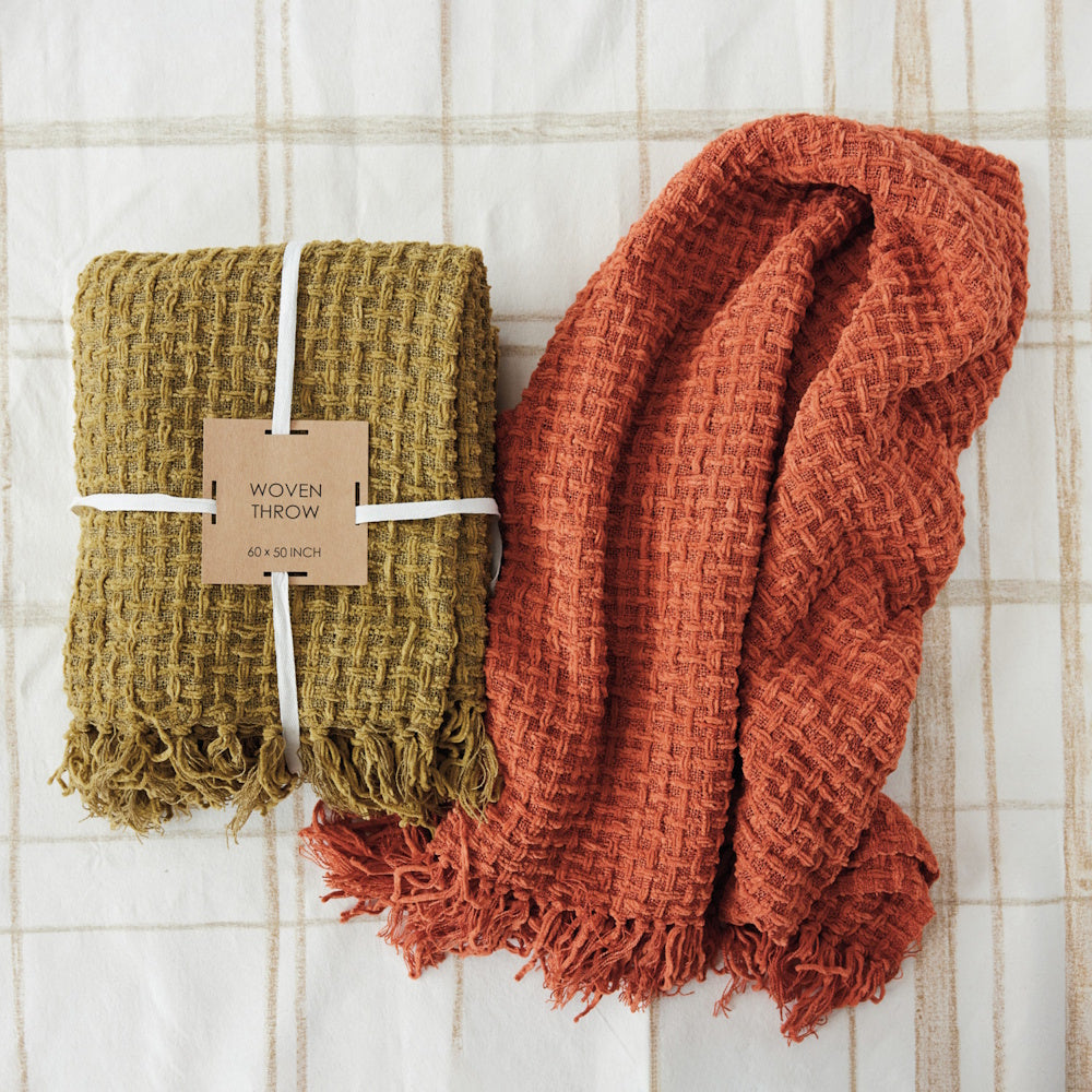 Folded mustard green and draped rust orange waffle-weave throw blankets with fringed edges.