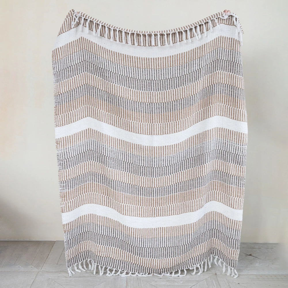 Woven neutral striped throw blanket with fringe and wavy chevron pattern, perfect for boho home decor.