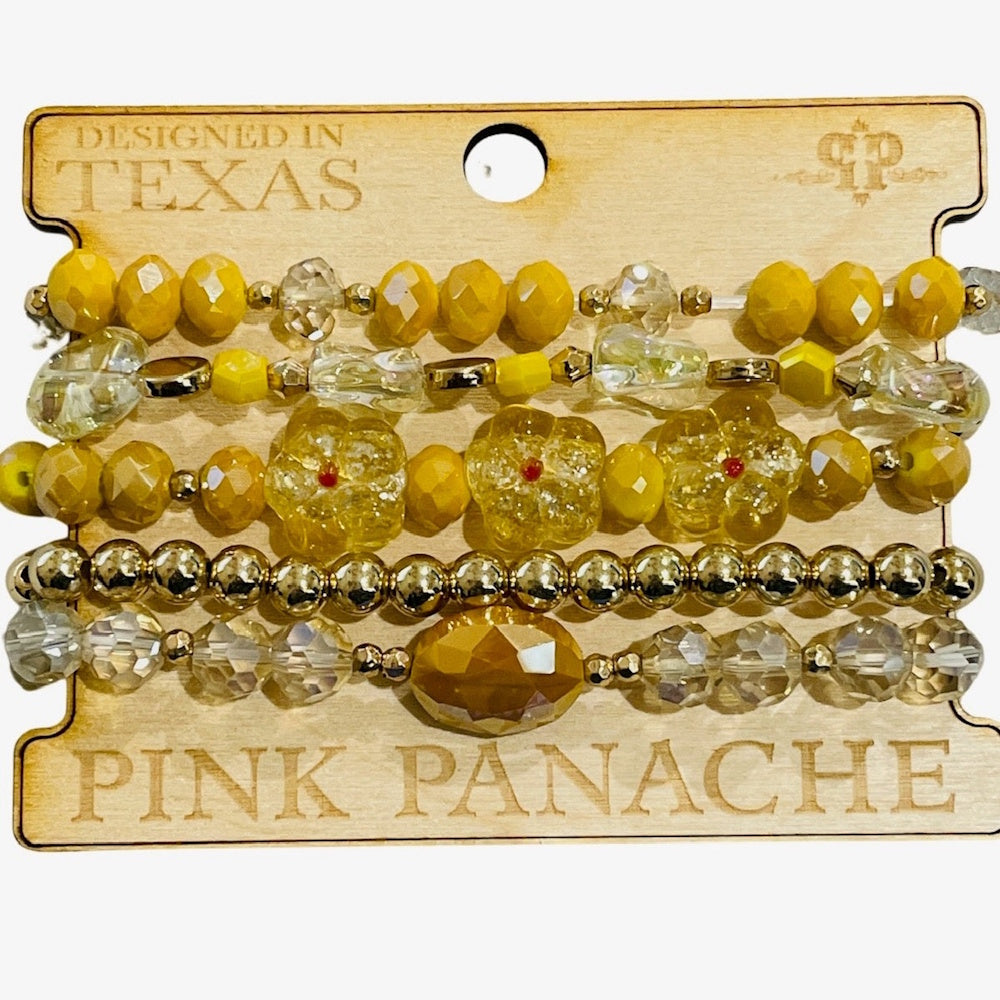 A stack of five yellow, clear, and gold beaded bracelets, featuring three clear flower charms, on a card.
