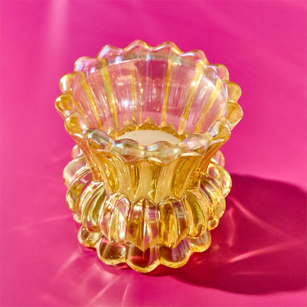 Yellow iridescent ribbed glass tealight holder or small bud vase set on a vibrant pink background.
